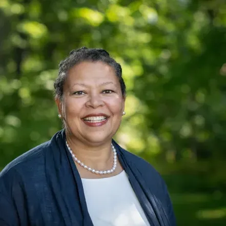 Photo of Sarah Willie-LeBreton smiling outdoors, in front of a background of green trees